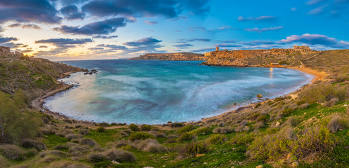 Fototapeta na wymiar Mgarr, Malta - Panoramic skyline view of the famous Ghajn Tuffieha bay at blue hour on a long exposure shot with beautiful sky and clouds