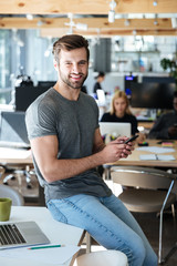 Happy young man sitting on table in office chatting