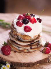 Delicious pancakes with berries and cream on the authentic wooden stand. Summer food still life concept.
