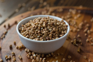 Buckwheat grain on ceramic bowl over wooden table.