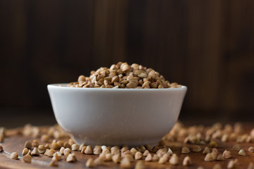 Buckwheat grain on ceramic bowl over wooden table.