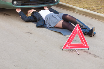 Woman, repairing broken car lying under it