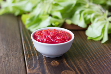 Mexican salsa or indian chutney in white ceramic bowl against green herbs