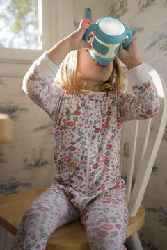 Girl sitting on chair and drinking milk from sippy cup