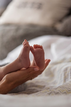Mother holding son's (0-1 months) feet in bedroom