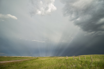 Sun rays radiate through the mist behind a passing storm on the prairie.