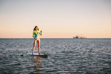 Attractive young girl stand up paddle surfing with beautiful sunset or sunrise colors