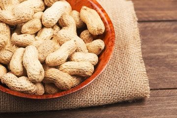 From above plate with whole peanuts on canvas bag. Wooden background. Horizontal studio shot.
