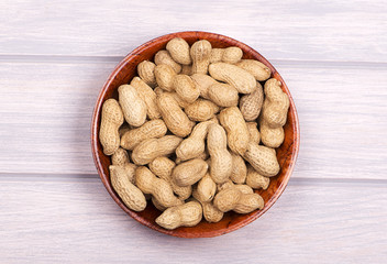 From above pile of whole peanuts in bowl on white wooden background.