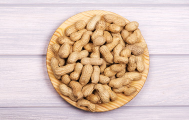 From above plate with whole peanuts on wooden background.