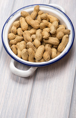 From above plate with whole peanuts on metal container, on wooden table. Copy space. Vertica studio shot.