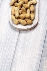From above plate with whole peanuts on wooden bowl, on wooden table.  Copy space. Vertical studio shot.