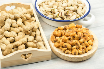 Peanuts, pistachios and toasted corn on a wooden tray next to toasted corn.