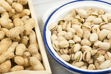 Peanuts, pistachios on a wooden tray next to toasted corn.