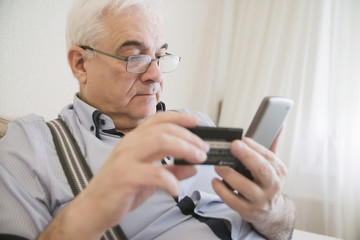 close-up adult gray-haired man holding a credit card and phone, it makes electronic payment