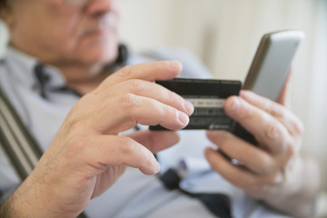 close-up adult gray-haired man holding a credit card and phone, it makes electronic payment