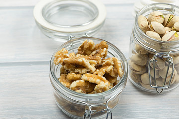 Walnuts and pistachios in glass containers on wooden table.