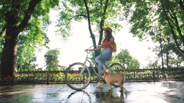 young beautiful woman standing with bicycle and her dog in a park