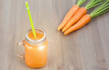 Healthy carrot smoothie in a mason jar with green parsley on wooden background