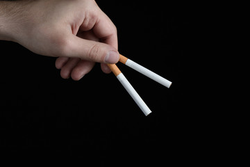 Male hand holding two fingers in the cigarette filters on black background