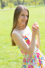 Portrait of young beautiful woman with long hair wearing flower dress in green spring park