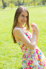 Obraz premium Portrait of young beautiful woman with long hair wearing flower dress in green spring park
