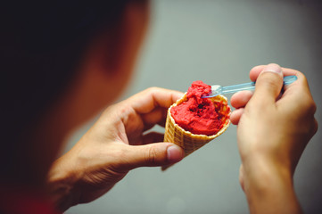 The hands of a man with an ice cream eat cherry ice cream in a waffle cup, a warm hot shot
