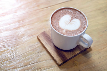 Hot chocolate with white heart shape latte art in white mug on wood table.