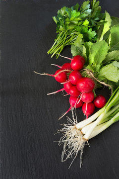 Ripe bunch red radish, onion, parsley with foliage on a black slate dish as background. Top view. Ingredients for salad.