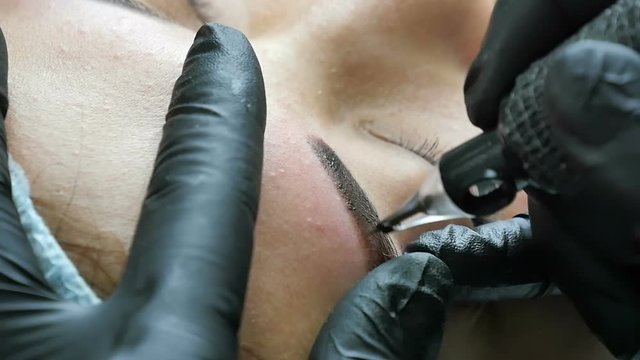 Master in gloves does tattoo of eyebrows close-up