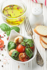 Traditional Italian Caprese salad with mozzarella, cherry tomatoes, Basil and balsamic vinegar in a white plate on the table. Selective focus