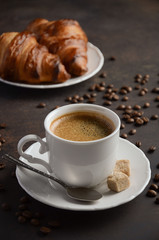 Cup of fresh coffee with croissants on dark background, selective focus