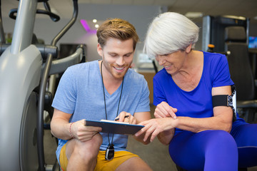 personal trainer assist senior woman exercising on machine at gym - Powered by Adobe