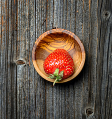 Strawberry in a bowl on a wooden table, top view