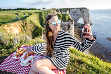 Young woman making selfie portrait with phone during the picnic outdoors sitting on the beautiful...