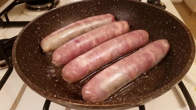 Appetizing ruddy juicy sausages fried in oil in a large frying pan