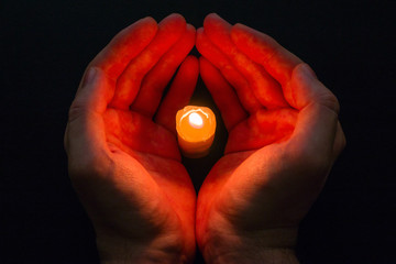 Two hands hold a candle in the dark. prayer.