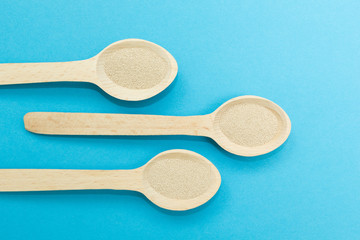 Three wooden spoons with instant dry yeast isolated on a blue background. Yeast is the main ingredient of fresh dough for pastry, pizza dough and many other dough.