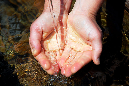 Hände schöpfen Wasser an einem Brunnen