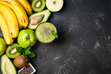 Healthy green smoothie and ingredients on dark background. Kiwi smoothie with fruits and chia seeds. Superfoods, diet, detox, health, vegetarian food concept