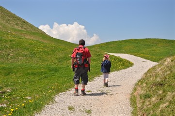 Vater mit Tochter am Wandern auf Wanderweg durch grüneWiesen und Hügellandschaft
