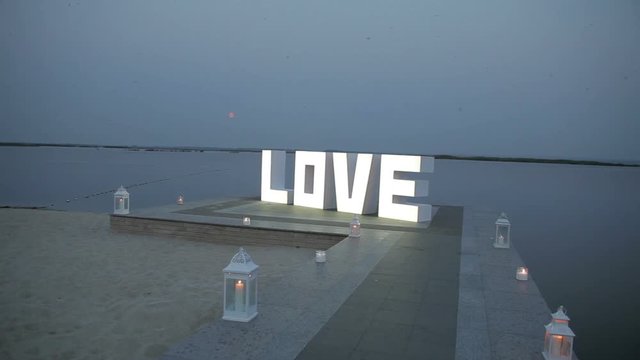 White letters forming word LOVE standing near river, the letters are illuminated at evening, LOVE letters standing at night, wedding decorations, valentines day.