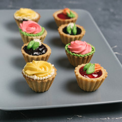 Row of colorful cupcakes on grey plate. Cakes with cream and jam on a stone background