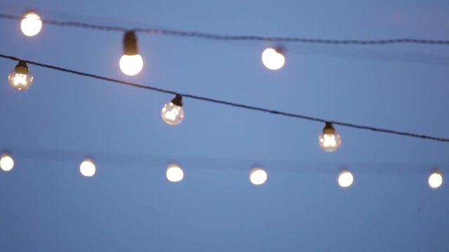 Light bulbs outdoor on a blue sky background, holiday concept, light bulbs and glow hang. lamp decoration garden at night, glass lantern. Many lamps collected in a garland.