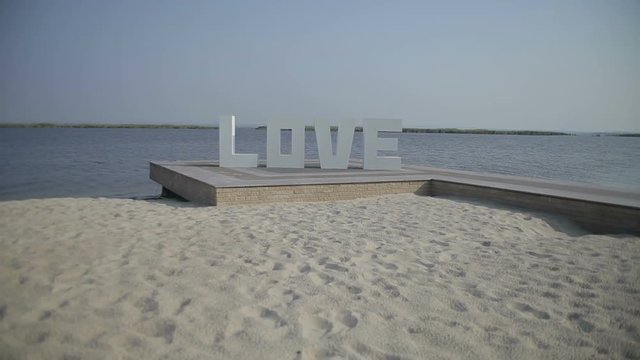 White letters forming word LOVE standing near river, LOVE letters, wedding decorations, valentines day. Steadicam shot.