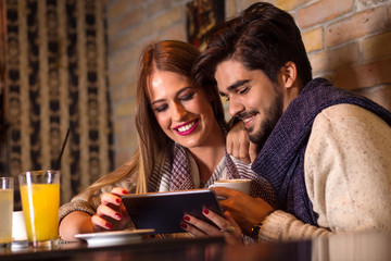 Beautiful young couple looking at tablet in cafe.