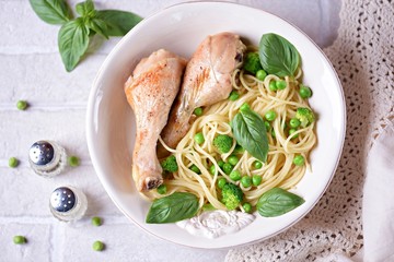 Baked chicken legs with pasta, green peas, broccoli and basil. Top view