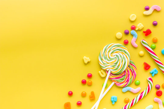 Sweets for birthday including lollipop and drops on yellow background top view copyspace