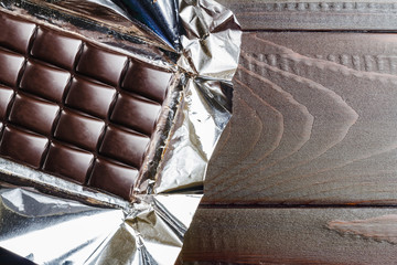Bitter, dark chocolate bar in foil on wooden background, top view