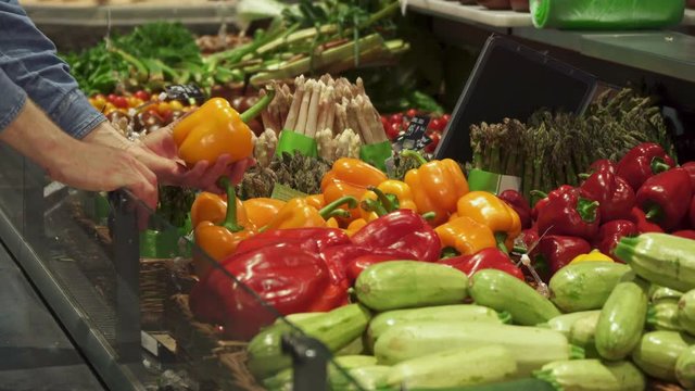 Low shot of man choosing between red and yellow bell pepers at the supermarket. Close up of male hands taking vegetables from the tray. Customer leaving one of products on the rack